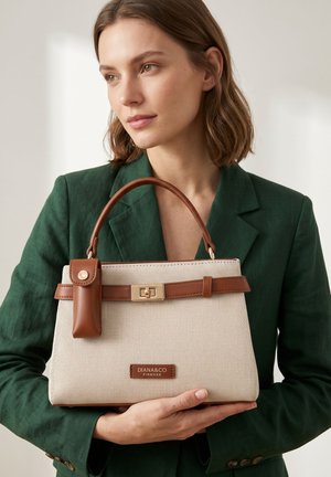 Femme en blazer vert tenant un sac à main beige et marron Diana&amp;Co Firenze avec poignée supérieure et fermeture à boucle.
