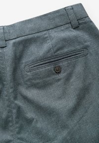 Tissu à motif sombre des pantalons sur mesure, présentant une poche arrière avec une fermeture à bouton noir. La texture est lisse avec un tissage subtil.