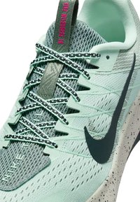 Jasnozielony but do biegania Nike z czarnym swooshem, wzorzystymi sznurowadłami i łachmaniaszowym ramieniem, podkreślający oddychającą siateczkę i projekt sznurowadeł.