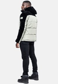 Vadderad jacka med huva och ärmar i svart sammet, ljusgrå kropp, dragkedjeficka på ärmen, bärs med svarta jeans och stövlar.