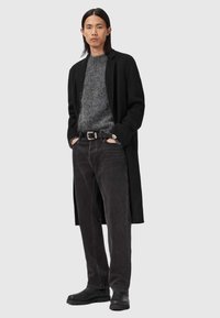 Palton lung negru peste un pulover texturat gri; blugi gri închis; curea neagră cu cataramă argintie; cizme negre; stil informal.