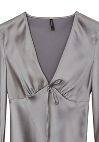Graues Satin-Oberteil mit V-Ausschnitt und Bindebanddetails an der Vorderseite. Lange Ärmel mit gerafften Akzenten, glatte Textur und taillierter Schnitt.