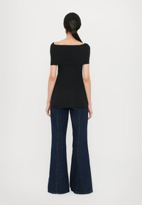Zwarte off-shoulder top in een aansluitend ontwerp, gecombineerd met high-waisted flared donkerblauwe jeans, met een gladde textuur en minimale details.