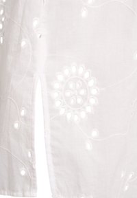 White cotton fabric featuring floral embroidery with cut-out details. Smooth texture with intricate stitching and design patterns throughout.