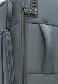 Grijze zachte koffer met een gladde textuur, dubbele ritsen met branding, meerdere compartimenten en een stevige handgreep voor gemakkelijk transport.