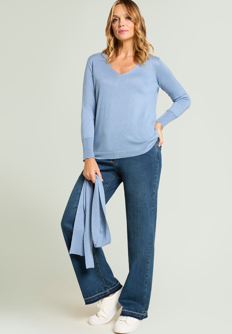 Jasnoniebieski sweter z dekoltem w serek wykonany z miękkiej dzianiny, zestawiony z szerokimi, ciemnoniebieskimi dżinsami oraz białymi trampkami, dopełniony dopasowanym szalikiem.