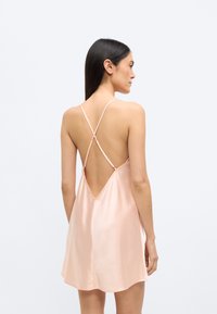 Φόρεμα slip από σατέν σε απαλό ροζ, με V-πλάτη και λεπτές, διασταυρούμενες τιράντες, καθώς και ρέον, ελαφρώς φαρδύ τελείωμα.
