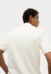 Ribbede, kortærmede polo t-shirt i off-white, med en klassisk krave og et tekstureret stof. Modellen vist fra ryggen.