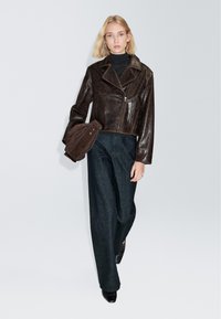 Braune kurze Lederjacke mit spitzem Kragen und Reißverschluss vorne, kombiniert mit dunklen, weit geschnittenen Denim-Hosen. Glatte Textur und klassisches Design.