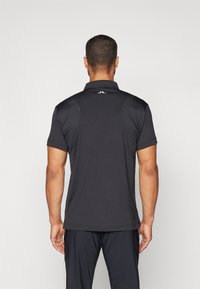 Black polo shirt made of breathable material, featuring short sleeves, a collar, and a subtle logo on the back. Smooth texture and regular fit.