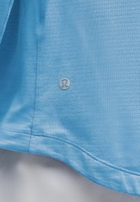 Lichtblauw sportshirt met een textuurstof, subtiele horizontale lijnen en een zilveren logo-detail nabij de zoom.