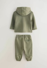 Felpa con cappuccio verde oliva con dettagli trapuntati sulle spalle e pantaloni abbinati con polsini elasticizzati e etichetta "ALLSAINTS" sul retro.
