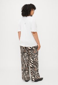 White short-sleeve blouse with back keyhole detail paired with wide-leg beige pants featuring black and brown zebra stripes. Black footwear.