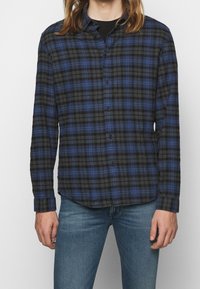 Svart och blå rutskjorta med långa ärmar och knappstängning, tillverkad av strukturerad tyg. Har en traditionell krage och rak fåll.