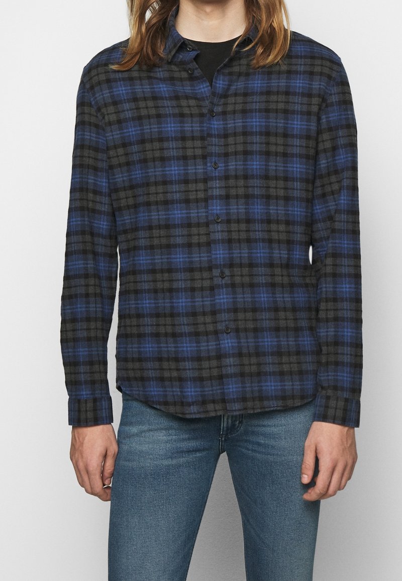 Svart och blå rutskjorta med långa ärmar och knappstängning, tillverkad av strukturerad tyg. Har en traditionell krage och rak fåll.