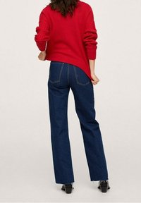 Pull rouge en tricot avec manches texturées, associé à un jean bleu foncé taille haute, jambes droites, avec ourlets effilochés et poches arrière.
