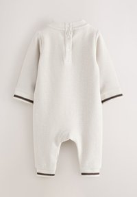 Vitt jumpsuit i våffelstruktur med långa ärmar, med en knappslå och randiga manschetter i marinblått och vitt. Mjukt tyg, avslappnad design.