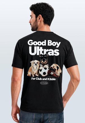 Man wearing black T-shirt with text "Good Boy Ultras For Club and Kibble" and three dogs with a soccer ball and shoe on the back.