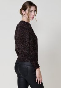 Schwarzer strukturierter Pullover mit mehrfarbigen Sprenkeln, rundem Halsausschnitt, langen Ärmeln und geripptem Saum, kombiniert mit schmalen schwarzen Hosen.
