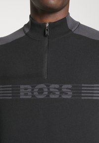 Czarny dzianinowy sweter z wysokim kołnierzem, z półsuwnym zamkiem błyskawicznym. Szare akcenty w okolicy ramion oraz logo "BOSS" w ciemniejszym odcieniu szarości na piersi.