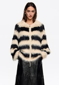 Nepbont jacket met afwisselende zwarte en crèmekleurige strepen, ritssluiting aan de voorkant en een ronde zoom. Heeft een zachte textuur en wijde mouwen.
