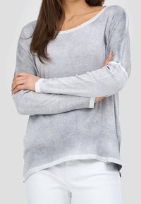 Ljusgrå långärmad topp med ribbat mönster, bred halsringning och vit kant. Bärs med vita byxor som har avslappnad passform och rundad nederkant.