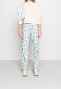 Felpa beige chiaro con spalle scese, abbinata a pantaloni a vita alta a quadretti blu chiaro e bianchi e stivaletti bianchi alla caviglia.