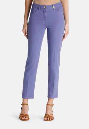 Lila Jeans im Slim-Fit-Stil, mit einem vorderen Knopfverschluss und fünf Taschen, kombiniert mit braunen Sandalen mit Riemen.
