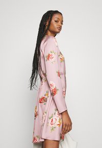 Vestido floral em tecido rosa, com mangas longas e cintura ajustada. Padrões de rosas bordadas em vermelho e amarelo, com uma saia rodada.