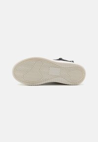 Czarny sneaker z teksturowaną gumową podeszwą z wzorem w zygzak oraz białą podeszwą środkową. System sznurowania widoczny na cholewce.