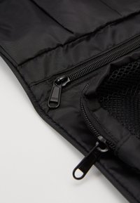Borsa nera imbottita con tessuto texturizzato, doppia cerniera e tasca in rete. Enfasi sulla finitura liscia e sui dettagli delle cuciture.