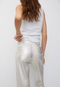 Metaliczne srebrne dżinsy z dwiema tylnymi kieszeniami, wysoki stan i gładka, błyszcząca textura, w połączeniu z dopasowanym białym tank topem.