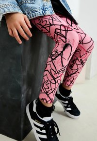 Rosa leggings med svarta abstrakta linjemönster, åtsittande design, matchande med svarta sneakers med vita ränder och en snördetalj.
