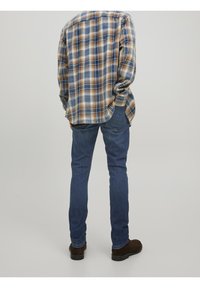 Rutigt flanellskjorta i blå, gul och brun nyanser, i kombination med smala blå jeans och bruna mocka anklarstövlar.