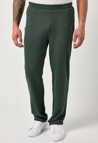 Pantalones de chándal verdes en una tela suave y texturizada con un corte relajado y cinturilla elástica, combinados con zapatillas blancas. Sin patrones visibles.