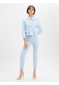 Lichtblauwe cropped jas met drie knopen, grote kraag en twee zakken, gecombineerd met bijpassende slim-fit broek en beige hakken.