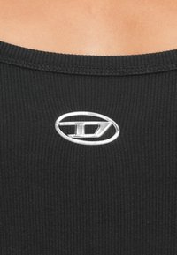 Μαύρο ριμπ τοπ με στρογγυλή λαιμόκοψη και ένα εντυπωσιακό ασημένιο οβάλ λογότυπο στο κέντρο μπροστά.