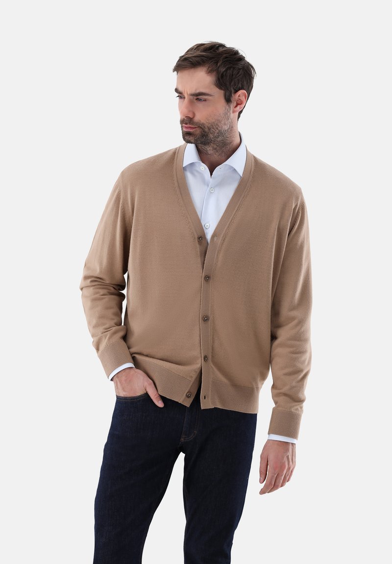 Hellbrauner Cardigan aus weichem Material mit V-Ausschnitt, fünf Knöpfen und gerippten Bündchen, kombiniert mit einem weißen Kragenhemd und dunklen Jeans.