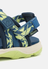 Sport sandaler med mörkblå och klargula mönstrade remmar, justerbara stängningar och en texturerad grön sula.