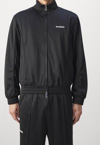 Black tracksuit in smooth fabric featuring a high collar, zip front, and elastic cuffs. Brand logo displayed on the chest and pants.