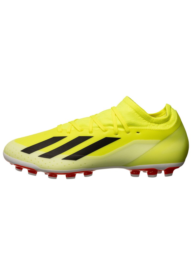 Botín de fútbol amarillo brillante con un diseño elegante, que presenta rayas negras, una puntera texturizada y tacos rojos sobre una suela blanca.