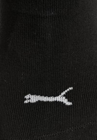 Calcetín de algodón negro con textura acanalada que presenta un diseño de logo en blanco de un gato saltando. Estilo simple y clásico.