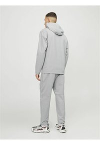 Sudadera con capucha gris y pantalones de chándal a juego. Tejido suave, corte relajado, puños acanalados y un bolsillo tipo canguro visible. El calzado presenta materiales mixtos.