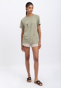 Olijfgroen katoenen T-shirt met een klimgraphic, ronde hals, korte mouwen, relaxte pasvorm, gecombineerd met lichtbeige shorts en zwarte sandalen.