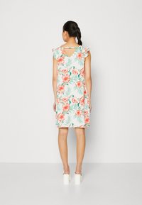 Blumenkleid mit weißem Hintergrund, verziert mit roten und rosa Hibiskusblüten sowie grünen Blättern. Rüschenärmel und ein V-Rücken-Design.