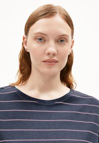 Marineblauwe T-shirt met roze horizontale strepen, ronde halslijn en zachte textuur. Model heeft halflang haar en een neutrale uitdrukking.