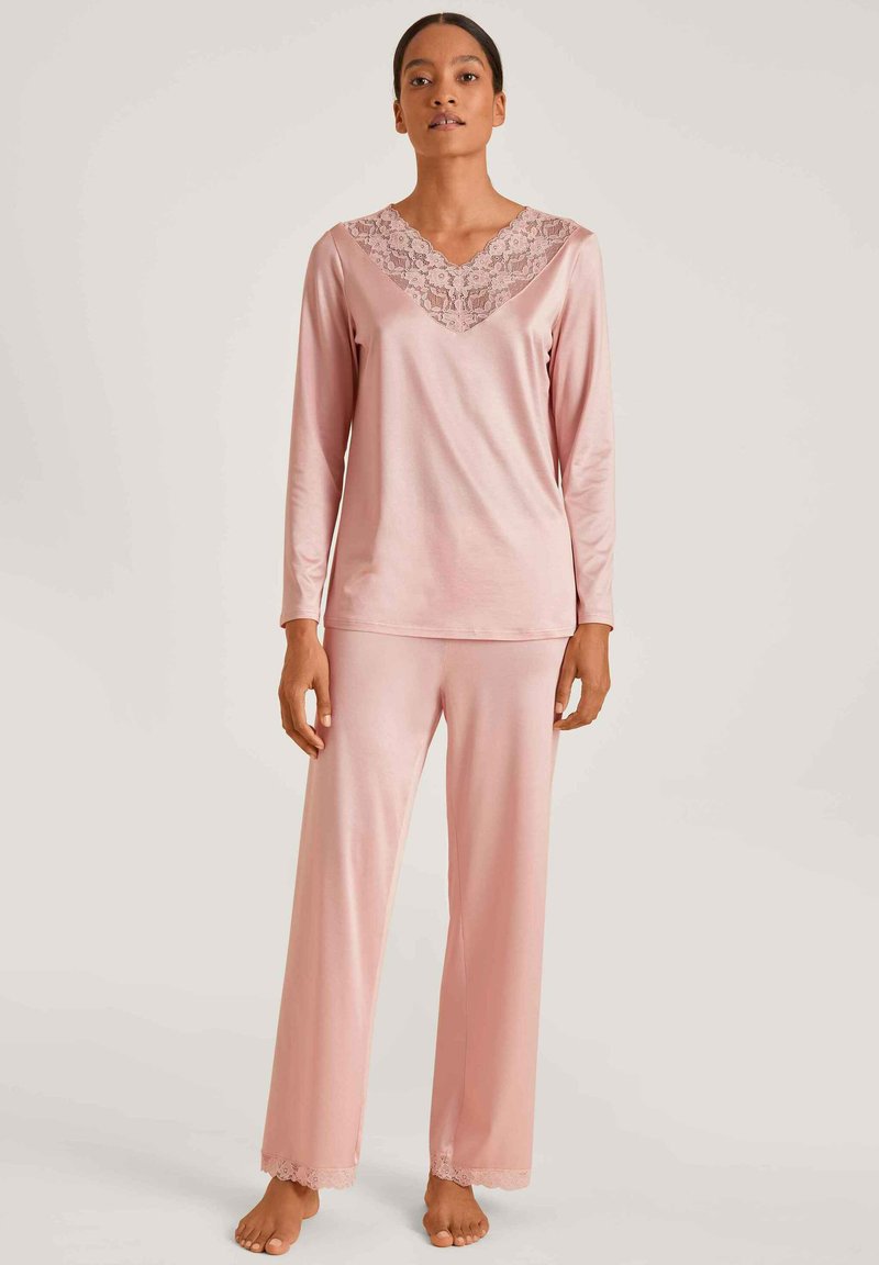 Lange mouwen, V-hals pyjamapakket in zachtroze stof. Kenmerkt kantafwerking op de halslijn en broekzoom, met een relaxte pasvorm en een gladde textuur.