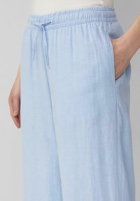 Hellblaue, weiche Stoffhose mit einem elastischen Taillenbund und Kordelzug, ausgestattet mit Seitentaschen und einem entspannten, weit geschnittenen Design.
