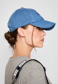 Blå denim tyg baseballkeps med justerbart band bak, med ventilationshål och en böjd skärm.