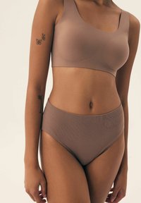 Brązowy stanik bezszwowy z szerokimi ramiączkami i gładką fakturą, w połączeniu z wysokimi majtkami bikini w dopasowanym odcieniu i prążkowanej tkaninie.